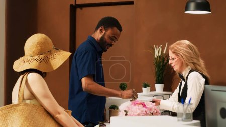 Photo for Hotel guests registering at reception, signing electronic check in forms on tablet at tropical resort. People on honeymoon vacation arriving at front desk lobby, hotel concierge. - Royalty Free Image