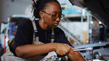 Photo for Certified technician in repair shop using torque wrench to tighten screws after checking car parameters during maintenance. African american expert using professional tool in garage to mend vehicle - Royalty Free Image
