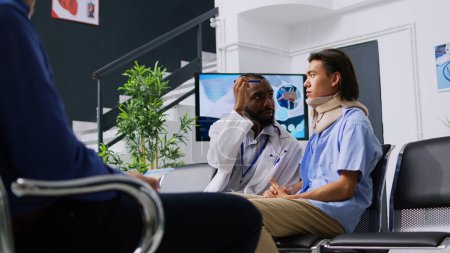 Photo for African american medic checking patient vision after medical surgery in hospital waiting room. Asian man wearing cervical neck collar discussing health care treatment with physician doctor - Royalty Free Image