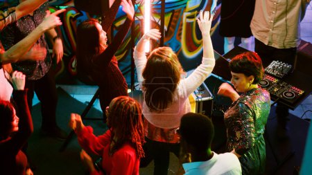 Foto de Grupo de jóvenes festejando en el club, divirtiéndose en pista de baile y bailando. Personas alegres disfrutando de la noche con música moderna y amigos, entretenimiento funky. Disparo de mano. - Imagen libre de derechos