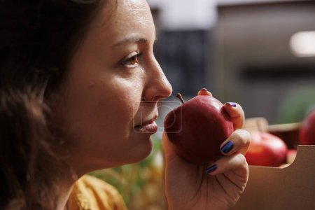 Téléchargez les photos : Femme sentant les pommes biologiques cultivées à la ferme dans un magasin zéro déchet à faible empreinte carbone. Test des clients pour voir si les fruits du quartier sont frais et exempts de pesticides, fermer - en image libre de droit