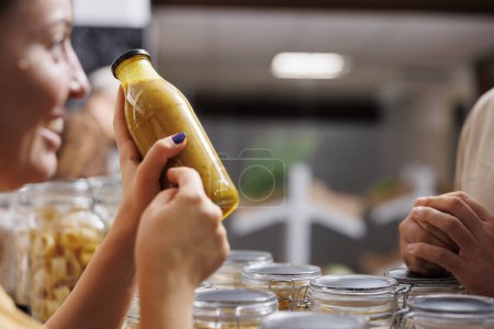 Photo for Vendor showcasing her products in zero waste marketplace venue, selling homemade fruit juice to interested customer, close up. Local farmer trading healthy food items during event, blurry background - Royalty Free Image