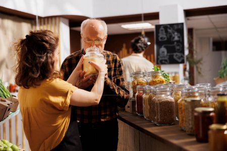 Photo for Vendor offering senior man product to smell in environmentally responsible zero waste store. Storekeeper helping client looking for pantry staples in eco friendly reusable packaging - Royalty Free Image