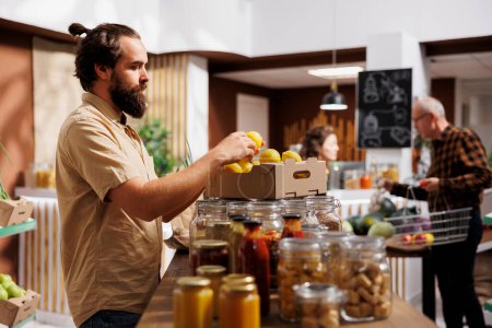 Photo for Man in zero waste store taking time to analyze fruits, making sure they are locally grown. Customer thoroughly checking local supermarket food items are ethically sourced - Royalty Free Image