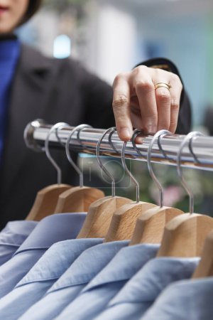 Photo for Shopping mall boutique seller hand adjusting and exploring apparel on rack closeup. Seller arm managing merchandise inventory and counting clothes in stock while working in outlet - Royalty Free Image