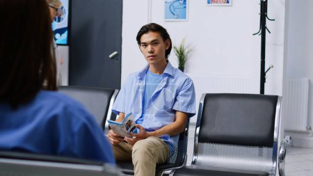 Téléchargez les photos : Portrait d'un patient asiatique attendant d'assister à une visite de contrôle avec un médecin, assis à la réception de l'hôpital. Homme malade se préparant à l'examen lors de la consultation de visite de contrôle. Concept de médecine - en image libre de droit