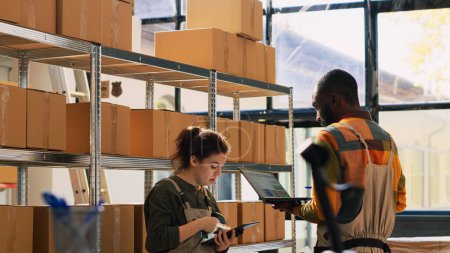 Photo for Storage room team verifying products in cardboard boxes, counting merchandise packages before shipping orders. Young diverse people working in storehouse, doing inventory. Handheld shot. - Royalty Free Image