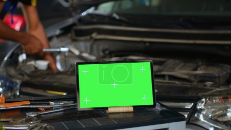 Photo for Close up shot of tablet placed on working bench in busy garage next to professional tools while technician mends vehicle. Mockup device in repair shop with meticulous specialist working in background - Royalty Free Image
