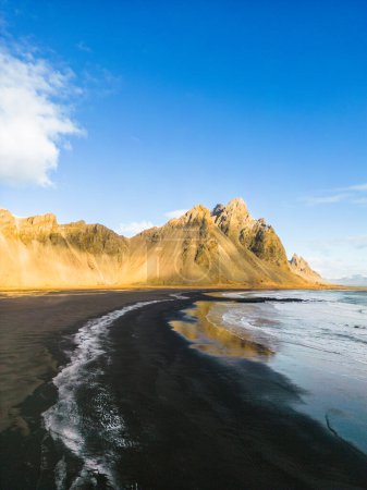 Foto de Paisaje del norte a lo largo de la orilla del océano con enormes picos de montaña Vestrahorn en Islandia. Famosa playa de Stokksnes con playa de arena negra icelándica y alrededores nórdicos, horizonte natural. - Imagen libre de derechos