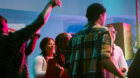Diverse people partying on disco music, having fun with stage lights and dance moves at nightclub. Happy adults enjoying social gathering with live performance on dance floor, entertainment.