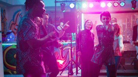 Téléchargez les photos : Groupe de personnes profitant d'une fête disco, dansant sur la musique du club lors d'un rassemblement social. Jeunes hommes et jeunes femmes dansant sur la piste de danse, faisant la fête avec des lumières de scène. Coup de main. - en image libre de droit