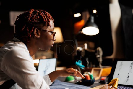 Photo for Close up of african american couturier wearing glasses looking online for fashion design inspirations. Seamstress in tailoring researching creative concepts for haute couture collection - Royalty Free Image