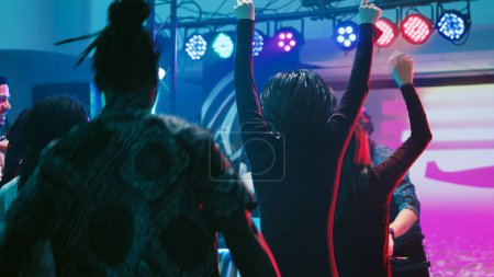 Photo for Diverse people jumping on dance music, feeling cheerful on dance floor at discotheque. Group of friends dancing on modern music with DJ mixing on stage, clubbing together. Tripod shot. - Royalty Free Image