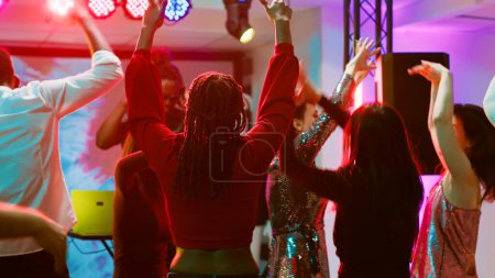 Photo for Funky persons dancing at nightclub, cheering for DJ and electronic music mix on stage. Group of people partying and jumping on dance floor with discolights and audio panel. Tripod shot. - Royalty Free Image