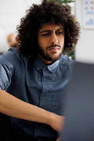 Téléchargez les photos : Jeune analyste financier arabe analysant les statistiques sur l'ordinateur portable dans le bureau d'affaires. Directeur exécutif de l'entreprise travaillant à la campagne de promotion des produits et vérifiant le rapport des ventes - en image libre de droit