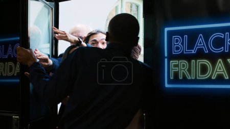 Photo for Crazy shoppers breaking down door during black friday promotions at clothing store, pushing security guard and forcing to enter retail shop boutique. Obsessed crowd of customers outdoors. - Royalty Free Image
