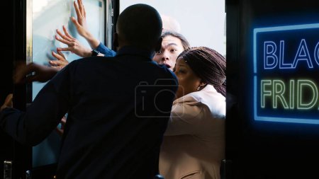 Photo for Security guard on black friday duty keeping people out of the clothing store, crazy customers being impatient about buying clothes on sale. Aggressive crowd of shoppers push door. Handheld shot. - Royalty Free Image