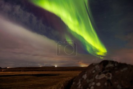 Foto de Al atardecer en Islandia, aurora boreal ilumina el cielo nocturno en tonos sobresalientes de verde y violeta, formando un mágico paisaje icelandés. Estrellas brillan alrededor de las luces del norte. - Imagen libre de derechos