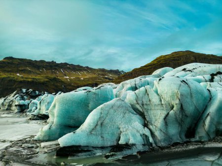 Téléchargez les photos : De magnifiques morceaux de glace aux tons bleu et vert apparaissent dans la masse majestueuse du glacier Vatnajokull, gelant les eaux froides de la côte islandaise. Drone shot de belle route avec des icebergs et de hautes falaises glacées. - en image libre de droit