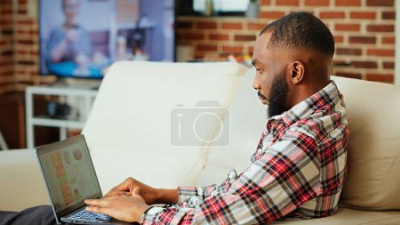 Photo for Remote employee using online analytics statistical data charts to identify trends and predict business outcomes. while working from home. Teleworker monitorizing market key performance indicators - Royalty Free Image