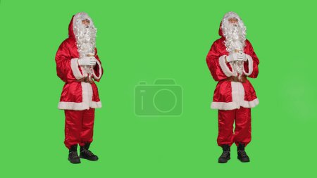 Photo for Santa claus drinks cup of hot chocolate in red festive winter costume with had and glasses, enjoying coffee beverage on greenscreen backdrop. Father christmas with seasonal refreshment. - Royalty Free Image