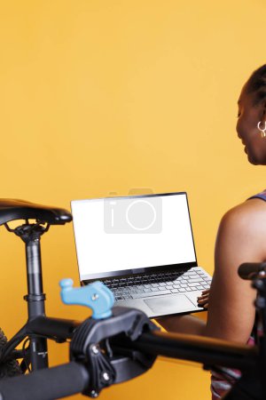 Photo for Close-up shot of laptop with isolated chromakey template carried by african american female. In front of yellow background, black person is holding wireless computer displaying blank whitescreen. - Royalty Free Image