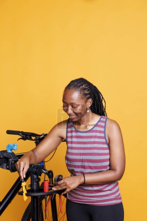 Téléchargez les photos : Photo montrant une femme noire saine et athlétique tenant des outils professionnels et se préparant à l'entretien annuel du vélo. Jeune femme plaçant du matériel spécialisé sur un support de réparation de vélos. - en image libre de droit