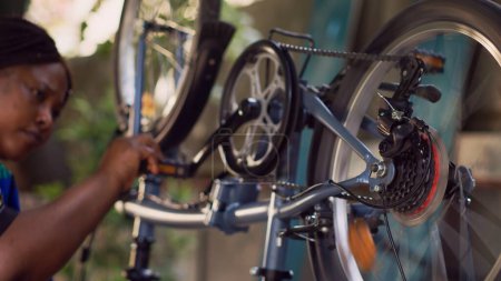 Photo for Skillful youthful black woman doing maintenance on bicycle confidently mending chain and inspecting crank arm. African american lady checking for damages to repair, close-up of bicycle parts. - Royalty Free Image