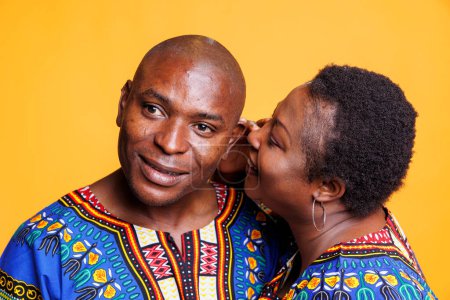 Téléchargez les photos : Couple afro-américain partageant le secret, exprimant amour et affection. Femme noire chuchotant à l'oreille du mari, racontant un message romantique privé sur fond de studio - en image libre de droit