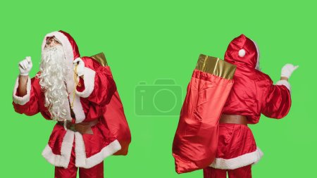 Photo for Saint nick bandmaster chief in costume accompany professional orchestra as choir musician, standing over greenscreen. Santa claus with gifts bag playing band music, musical conductor. - Royalty Free Image
