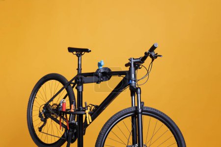 Photo for View of bicycle on repair-stand surrounded by specialized equipment outside for maintenance and repair. Modern damaged bike for repairing and adjusting, positioned in front of yellow background. - Royalty Free Image