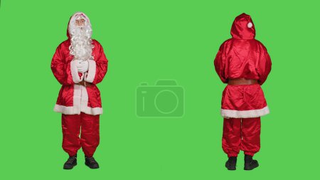 Photo for Man acting like santa in costume saying ho ho ho, portraying december famous character for christmas eve celebration. Saint nick with hat and beard standing over full body greenscreen. - Royalty Free Image