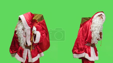 Téléchargez les photos : Homme habillé comme le Père Noël avec un sac rouge portant des cadeaux pour les enfants, portant un costume de fête et une barbe blanche pour l'esprit des fêtes. Caractère d'hiver célébrant la veille de Noël, Noël traditionnel. - en image libre de droit