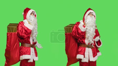 Photo for Santa claus cosplay shows marketing ad against greenscreen backdrop, posing with bag of gifts to advertise winter holiday season with main character. Father christmas red costume. - Royalty Free Image