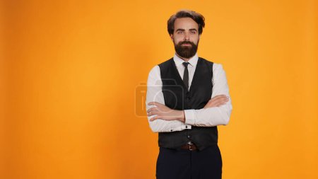 Photo for Restaurant waiter strikes air of optimism in studio as he prepares to serve consumers at table. Gentleman providing premium deluxe valet services while working in fine dining cuisine field. - Royalty Free Image