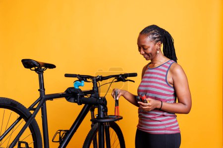 Foto de Atlética mujer afroamericana utilizando una variedad de herramientas para arreglar y mantener la bicicleta moderna. Mujer negra amante de los deportes reúne herramientas expertas para reparar bicicleta rota contra fondo aislado. - Imagen libre de derechos