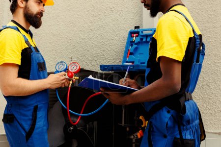 Photo for Seasoned specialists employed to do air conditioner check, refilling freon. African american engineer and coworker using manifold gauges to perfectly measure the pressure in condenser - Royalty Free Image