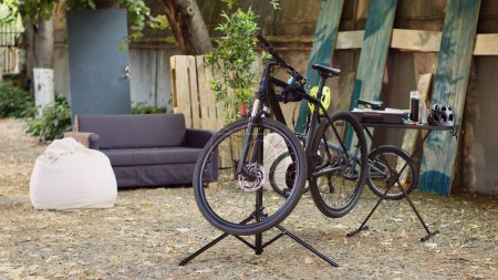 Photo for Bicycle resting on workstand with specialized tools tailored for precise adjustments. Setting provides glimpse of yard with broken bike awaiting repair and restoration to proper working condition. - Royalty Free Image