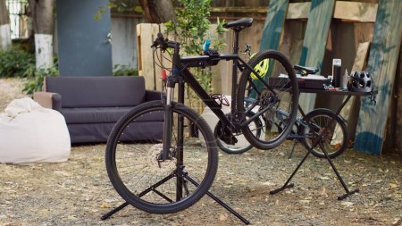 Photo for Damaged bike in home yard awaiting repair and maintenance, ready for summer cycling. View of modern bicycle positioned on repair-stand for further adjustments outdoors. - Royalty Free Image