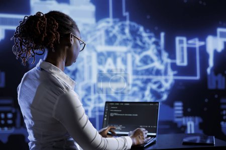 Photo for African american engineer updating AI systems, writing intricate binary code scripts on laptop. Tech support using programming to upgrade artificial intelligence simulation model - Royalty Free Image