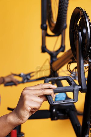 Photo for Close-up shot of african american individual fixing a bicycle and doing routine maintenance. Detailed image showcasing a pair of hands repairing and adjusting bike pedals for recreational cycling. - Royalty Free Image