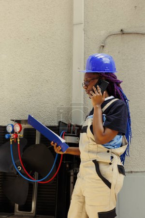 Photo for Precise technician apprentice offering informations about air conditioner needing to be replaced to master over the phone. Engineer checking maintenance plan after fixing faulty compressor - Royalty Free Image