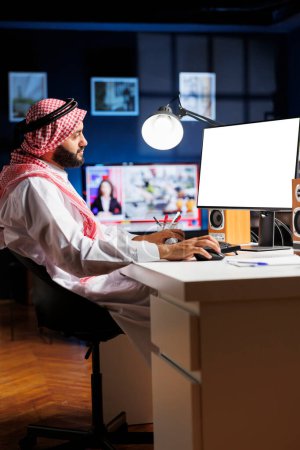 Téléchargez les photos : L'image montre un homme islamique assis à son bureau à domicile avec le moniteur PC de bureau affichant un modèle d'espace de copie vierge. Dédié arabe gars en utilisant l'ordinateur ayant un écran blanc isolé. - en image libre de droit