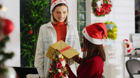 Photo for Asian employee surprised by supervisor with thoughtful Christmas gift in festive ornate workplace. Company director offering worker xmas present during winter holiday season - Royalty Free Image