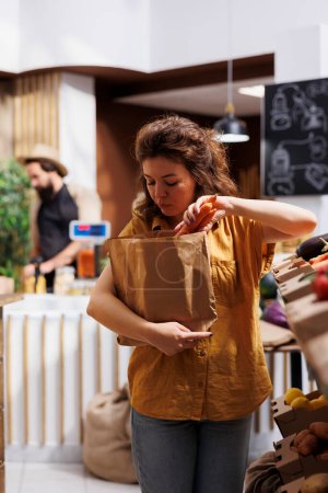 Photo for Woman in zero waste shop purchasing natural greenhouse grown vegetables, picking ripe carrots. Client in plastic free local grocery shop looking to buy healthy food, using nonpolluting paper bag - Royalty Free Image