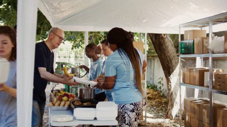 Photo for At food drive, organized by non-profit, gathers diverse group of individuals committed to aiding the homeless and less fortunate. Volunteers generously provide hot meals to those in need. Handheld - Royalty Free Image