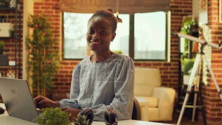 Téléchargez les photos : Pigiste afro-américain à partir de la journée à la maison, résoudre des tâches pour le projet e-business. Femme travaillant sur un ordinateur portable et répondant à des courriels au bureau, blogueur indépendant télétravailleur. - en image libre de droit