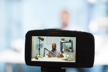 Téléchargez les photos : Blogger streaming tout en créant du contenu numérique et en enregistrant des vidéos avec une caméra professionnelle en gros plan. Vlogger afro-américain enregistrement vidéo et diffusion en direct pour podcast - en image libre de droit