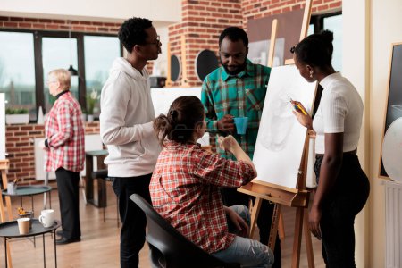 Foto de Jóvenes amigos tomando clases de dibujo en un estudio de arte, asistiendo juntos a un taller creativo. Grupo de estudiantes afroamericanos hombres y mujeres escuchando al maestro, aprendiendo técnicas de dibujo - Imagen libre de derechos