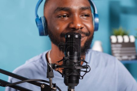 Téléchargez les photos : Homme afro-américain dans les écouteurs parlant au microphone tout en diffusant podcast. Jeune blogueur portant un casque parlant en micro lors de l'enregistrement de contenu vidéo numérique gros plan - en image libre de droit
